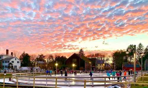 A vibrant sunset over an outdoor ice skating rink with people skating and colorful clouds in the sky.