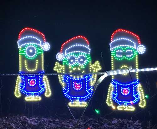 Three illuminated Minion characters wearing Santa hats, surrounded by colorful lights against a dark background.