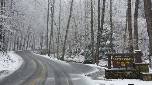 Snowy road leading to Carter Caves State Resort Park, surrounded by trees in a winter landscape.