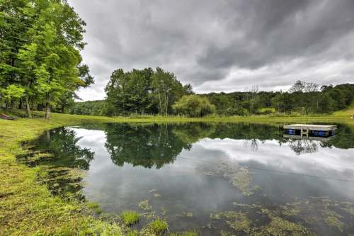 A serene pond surrounded by lush greenery under a cloudy sky, reflecting the landscape in calm waters.