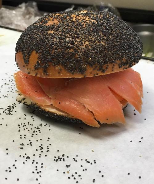 A poppy seed bagel filled with layers of smoked salmon on a white surface.