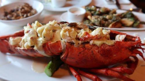 A close-up of a lobster dish, featuring a lobster tail stuffed with creamy filling, served with sides.
