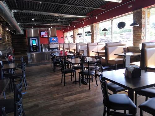 Interior of a casual restaurant with wooden floors, booths, and tables, featuring a drink station and large windows.