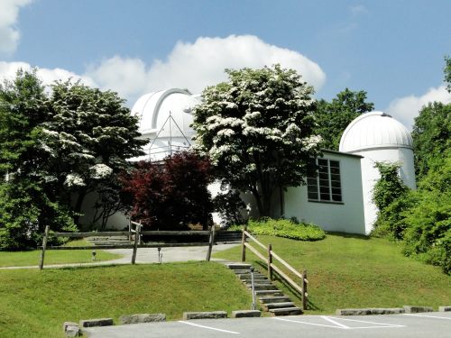 A white observatory building surrounded by trees and greenery under a blue sky with fluffy clouds.