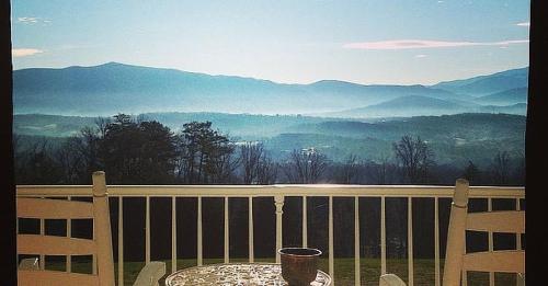 A serene view of misty mountains from a balcony, with a table and a small pot in the foreground.