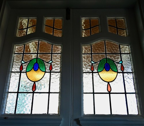 Stained glass doors featuring colorful designs with circular and teardrop patterns, illuminated by natural light.
