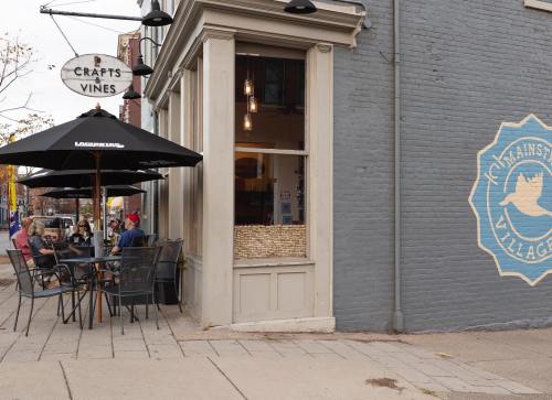 A cozy outdoor dining area with tables under umbrellas next to a gray building featuring a sign for "Crafts & Vines."