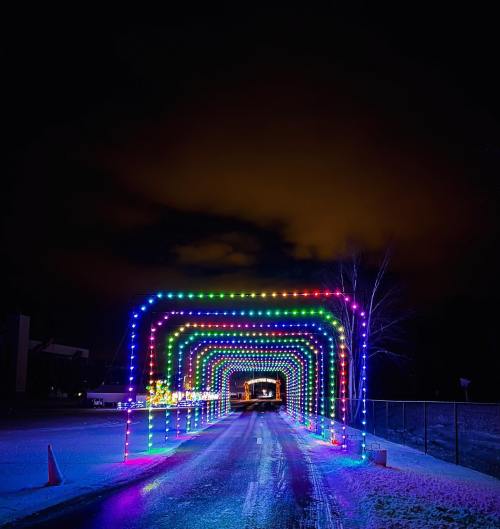 A colorful light tunnel arches over a snowy road at night, creating a festive atmosphere.