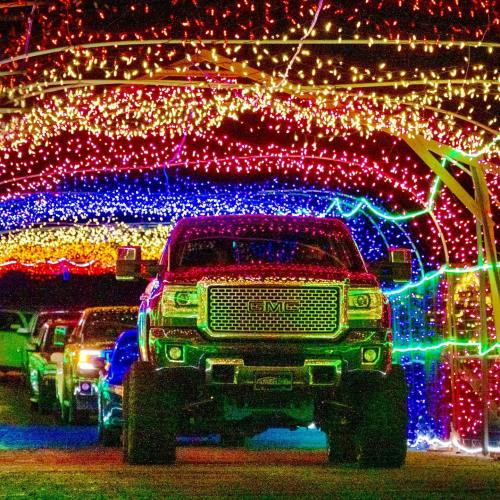 A truck drives through a colorful, illuminated tunnel of festive lights at night.