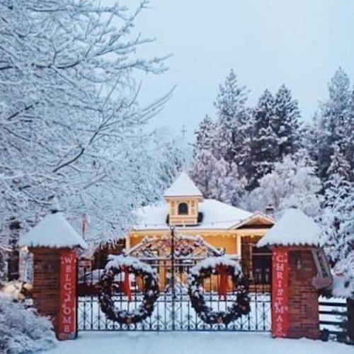 A snowy scene featuring a charming house with a festive entrance adorned with wreaths and a "Welcome to Christmas" sign.