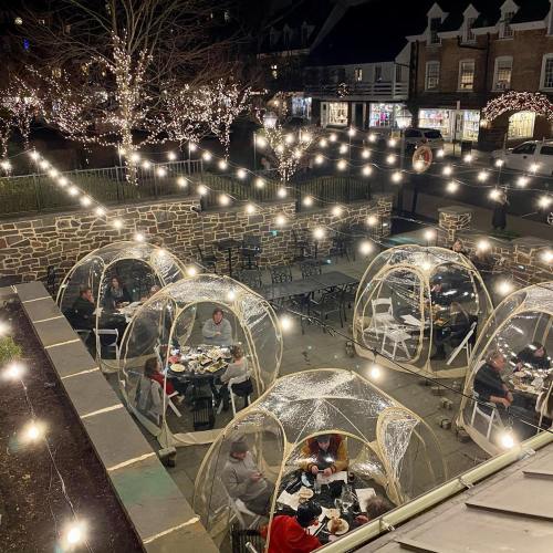 Outdoor dining area with transparent igloos, string lights, and patrons enjoying meals in a festive atmosphere.