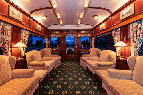 Cozy train interior with plush armchairs, warm lighting, and floral curtains, creating an inviting atmosphere.