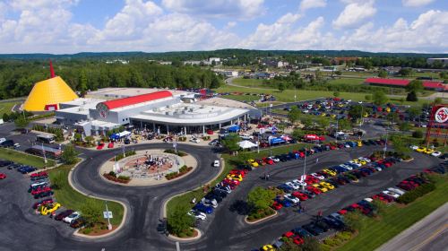 Aerial view of a busy car show at a large venue, featuring colorful cars parked around a circular drive.