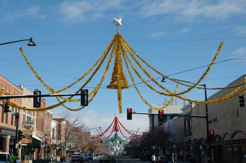 A festive street scene decorated with golden tinsel and a star, under a clear blue sky.