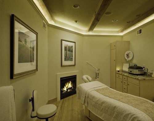 A serene spa room with a massage table, fireplace, and calming decor, featuring soft lighting and nature-themed artwork.