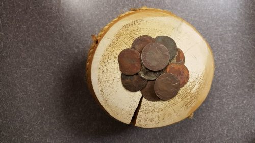 A collection of old coins arranged on a wooden stump with a visible crack in the surface.