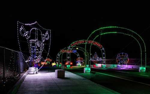 Colorful holiday lights create festive arches along a pathway at night, with various Christmas-themed decorations.