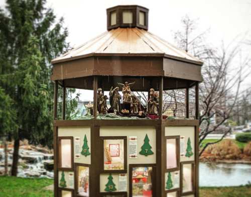 A decorative gazebo featuring a nativity scene, surrounded by trees and a serene outdoor setting.