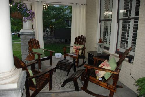 A cozy porch with wooden chairs, cushions, a small table, and a lantern, surrounded by greenery.