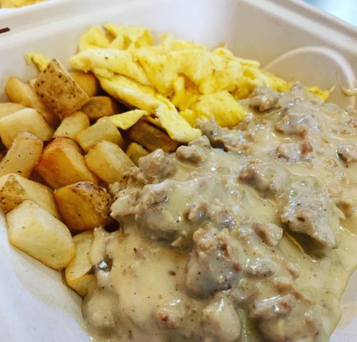 A takeout container with scrambled eggs, diced potatoes, and sausage gravy over biscuits.