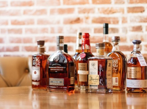A selection of whiskey bottles displayed on a wooden table against a brick wall background.