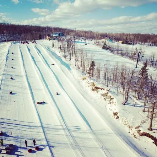 A snowy landscape with multiple tubing lanes and people enjoying winter activities under a clear blue sky.