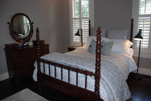 Cozy bedroom featuring a wooden four-poster bed, dresser, mirror, and soft lighting from two lamps.