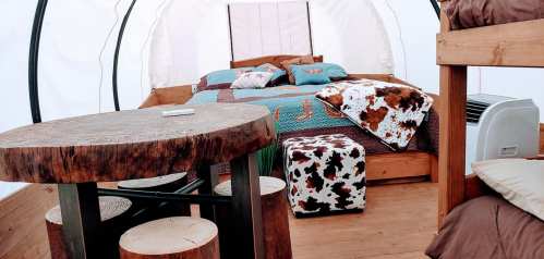 Cozy glamping tent interior with a double bed, bunk beds, wooden table, and decorative blankets.