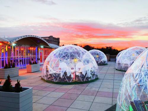 Clear igloos on a rooftop terrace at sunset, with colorful lights and a vibrant sky in the background.