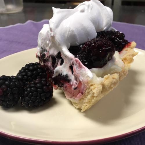 A slice of dessert with layers of blackberries, whipped cream, and a flaky crust, served with fresh blackberries on the side.