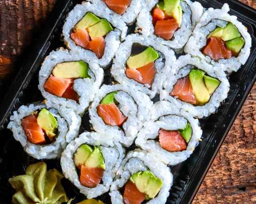 A close-up of a sushi platter featuring rolls with salmon and avocado, arranged neatly in a black container.