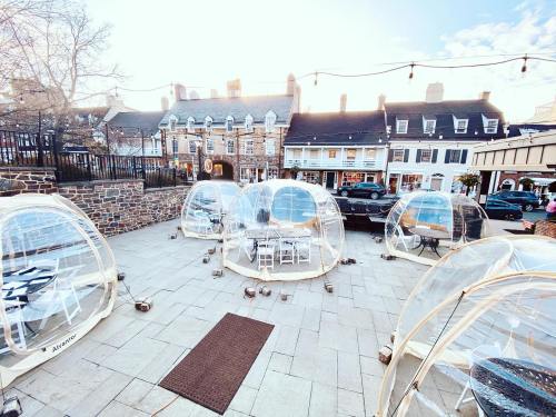 Outdoor dining area with transparent igloo-like pods on a paved surface, surrounded by buildings and string lights.