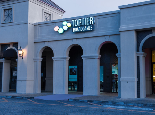 Exterior of Top Tier Boardgames store, featuring a sign and arched entryway, illuminated in the evening light.