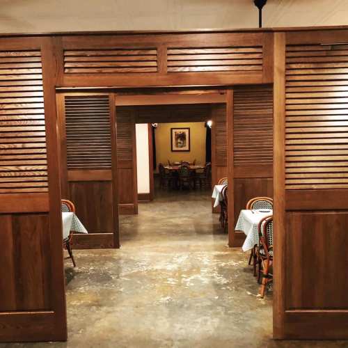 Interior of a restaurant featuring wooden partitions, tables with checkered tablecloths, and warm lighting.