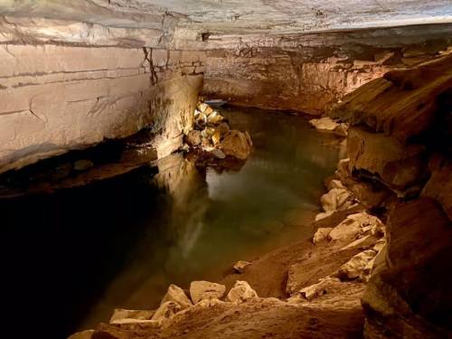 A serene underground cave with a calm water pool reflecting the rocky walls and ceiling.