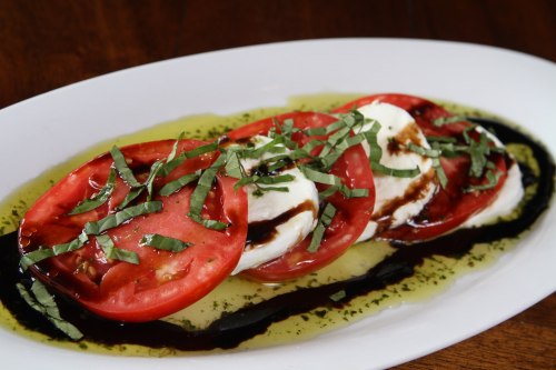 A plate of caprese salad featuring sliced tomatoes, mozzarella, basil, and drizzled with balsamic glaze.