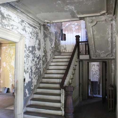 A worn staircase in an old, peeling interior with faded walls and a vintage railing.