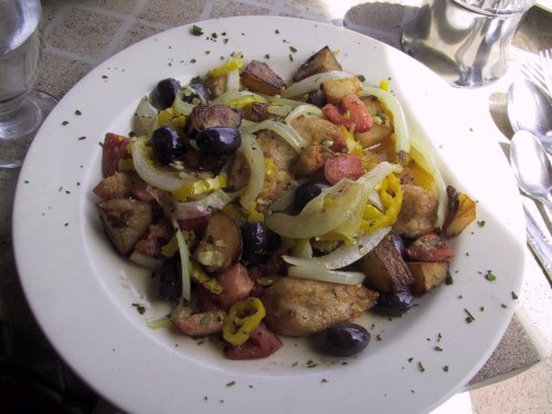 A colorful plate of sautéed vegetables, olives, and fried potatoes, garnished with herbs.