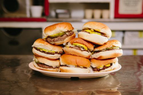 A stack of delicious burgers with pickles and mustard on a plate, set on a shiny metal surface.