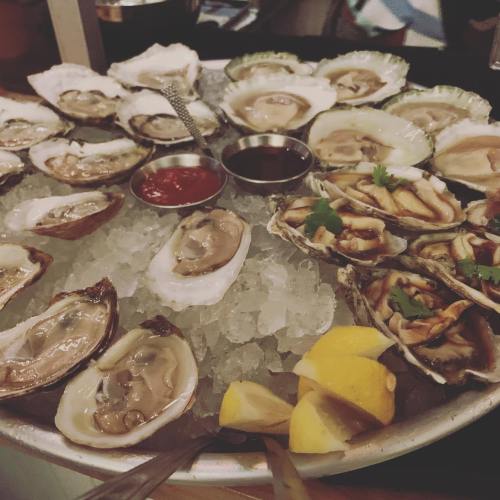 A platter of fresh oysters on ice, garnished with lemon wedges and served with dipping sauces.