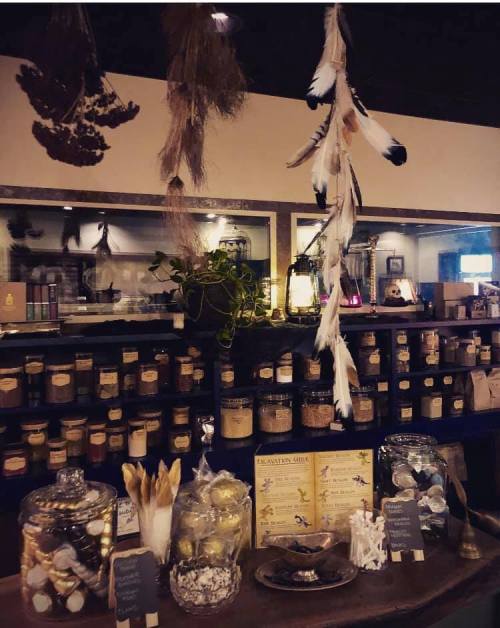 A cozy shop display featuring jars of herbs, feathers hanging, and decorative items on a wooden table.