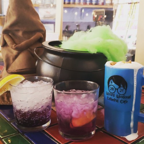 Two colorful cocktails with ice, a cauldron with green cotton candy, and a themed cup on a vibrant tiled surface.