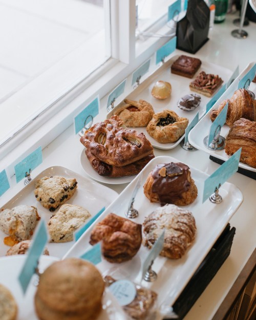 A display of various baked goods, including pastries and cookies, arranged on white trays with labels.