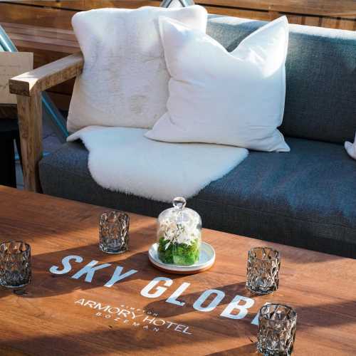 A cozy seating area with pillows, a glass terrarium, and decorative candles on a wooden table featuring "SKY GLOBE."