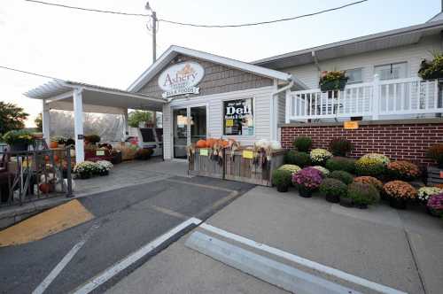 A charming market entrance with pumpkins and colorful mums outside, featuring a sign for local foods.