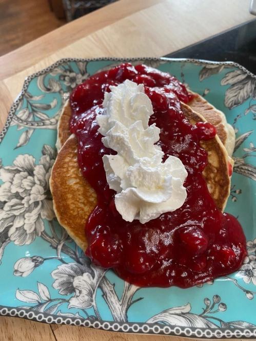 Two pancakes topped with cherry sauce and whipped cream, served on a decorative blue floral plate.