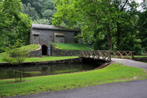 A stone building surrounded by greenery, with a small pond and a wooden bridge in front.