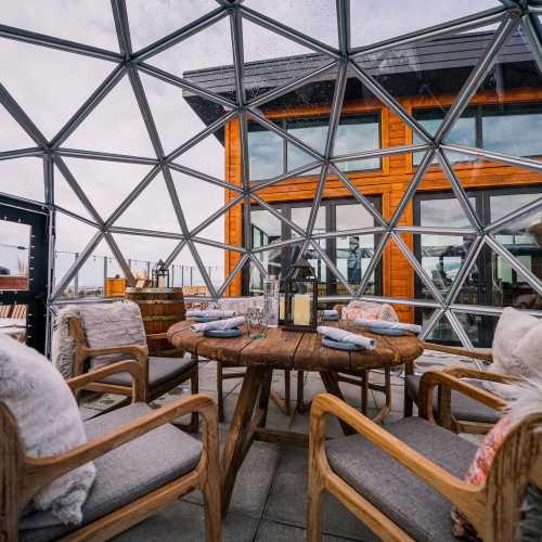 A cozy dining area inside a geodesic dome, featuring wooden furniture and large windows with a scenic view.