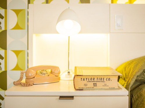 A bedside table with a vintage lamp, a rotary phone, and a yellowed book titled "TAYLOR TIRE CO. (INCORPORATED)."