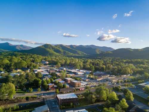 Aerial view of a small town surrounded by lush green mountains under a clear blue sky.